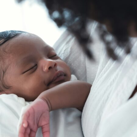 Close up portrait of cute African american newborn infant baby lying in mother's arms at hospital.