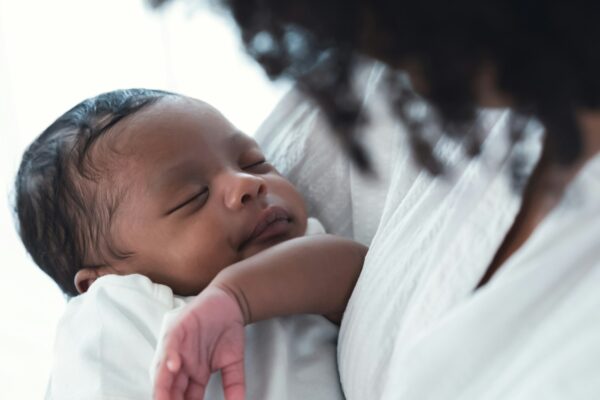 Close up portrait of cute African american newborn infant baby lying in mother's arms at hospital.